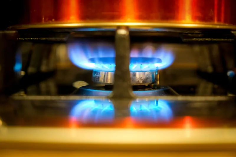 Close-up of a blue flame on a gas stove burner, showcasing kitchen heat and cooking