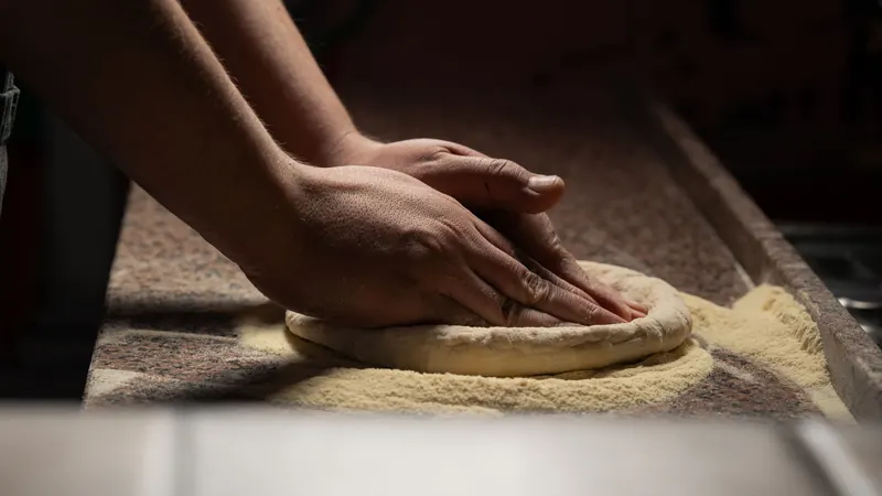 Close-up of hands kneading pizza dough on a floured countertop, indoors