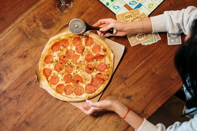 Top view of a pepperoni pizza and board game setup on a wooden table, perfect for a cozy night in