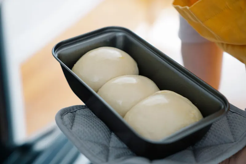 Close-up of dough balls in a baking tray held with an oven mitt, ready for baking