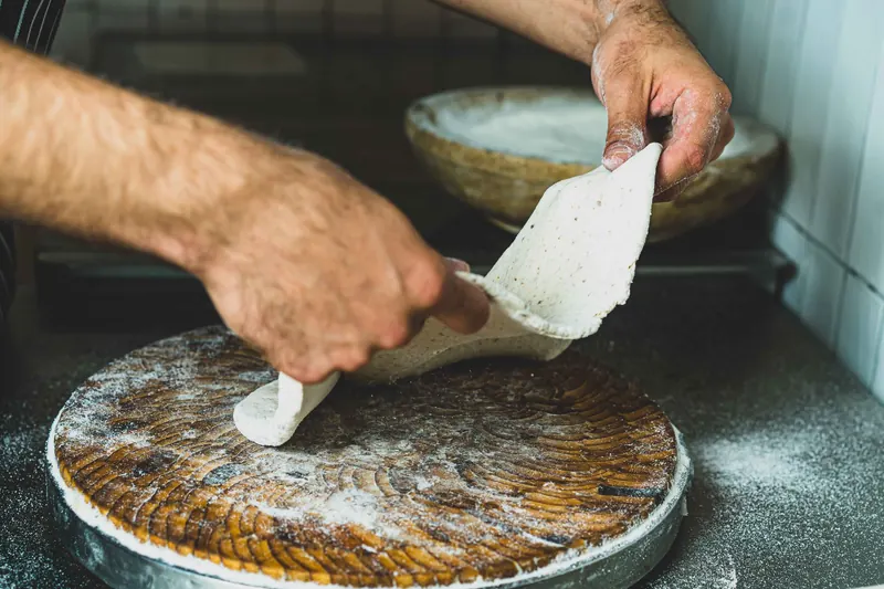 Hands of a chef shaping pizza dough on a wooden board in a kitchen setting