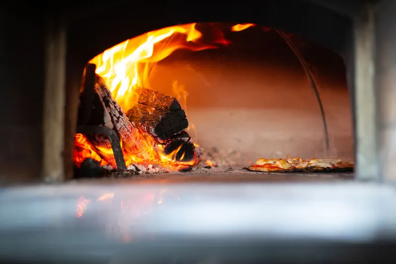 Authentic pizza baking with open flames in a traditional wood-fired oven, creating a rustic gourmet experience