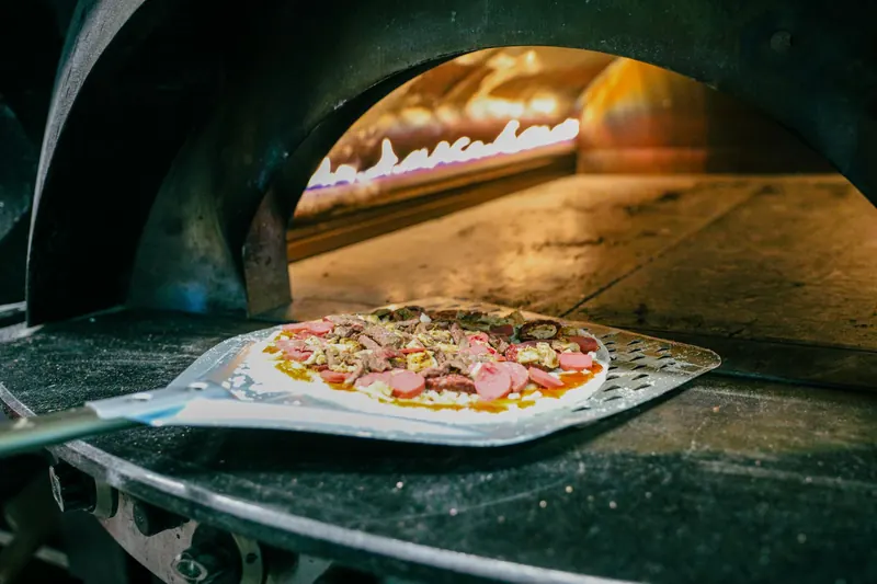 Fresh pizza being prepared in a traditional wood-fired stone oven, capturing authentic Italian cooking