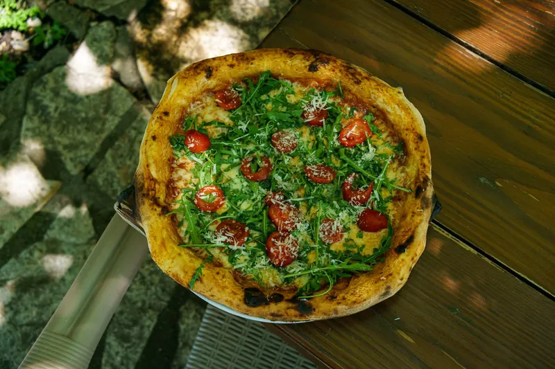 Tasty pizza topped with fresh arugula and cherry tomatoes on a sunny outdoor table