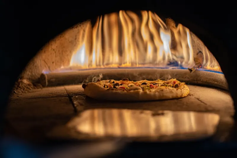 A delicious pizza baking in a traditional wood-fired oven with vibrant flames