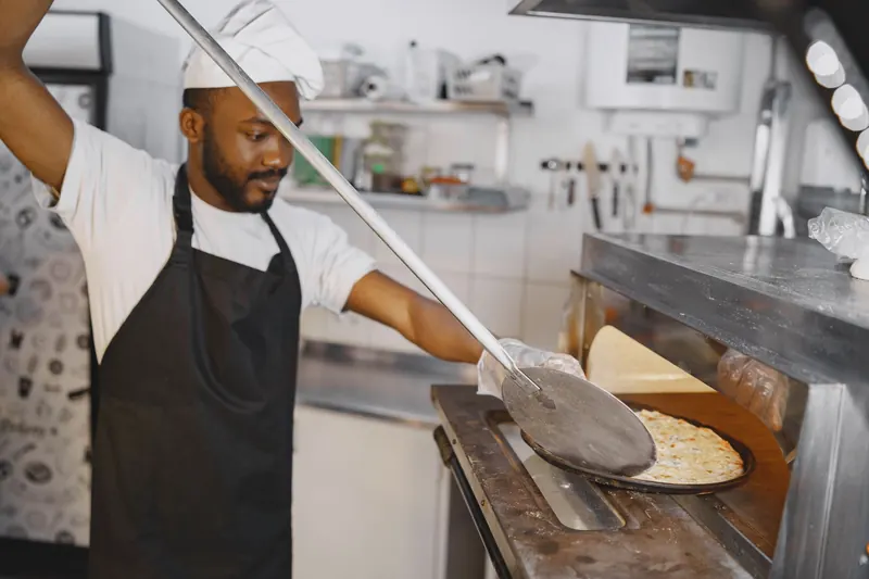 A skilled chef using a pizza peel to place a delicious pizza in a traditional oven