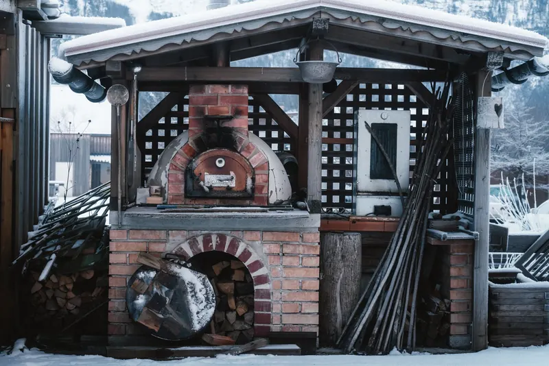 Brick pizza oven surrounded by snow, evoking a rustic alpine retreat feel