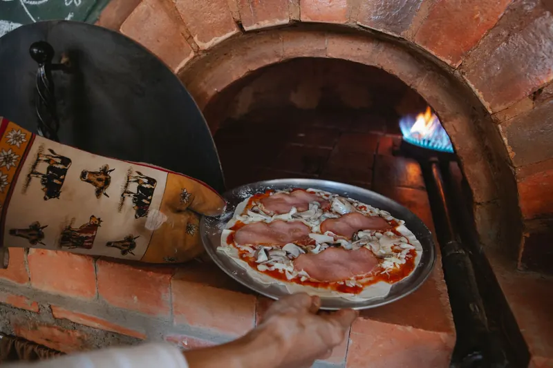 A delicious pizza with ham and cheese being baked in a traditional wood-fired oven
