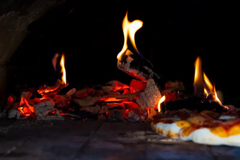 A close-up of a stone oven with bright flames, showcasing the baking process of a pizza
