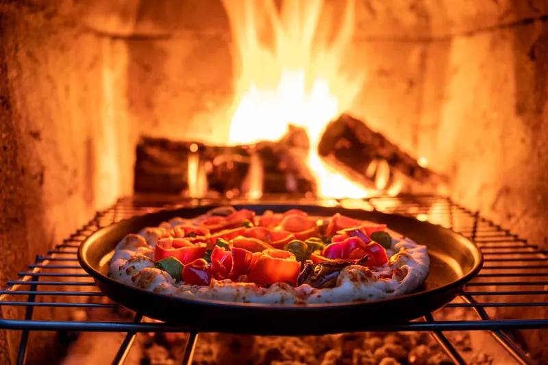 Freshly prepared pizza baking in a wood-fired oven with vibrant toppings and a crispy crust